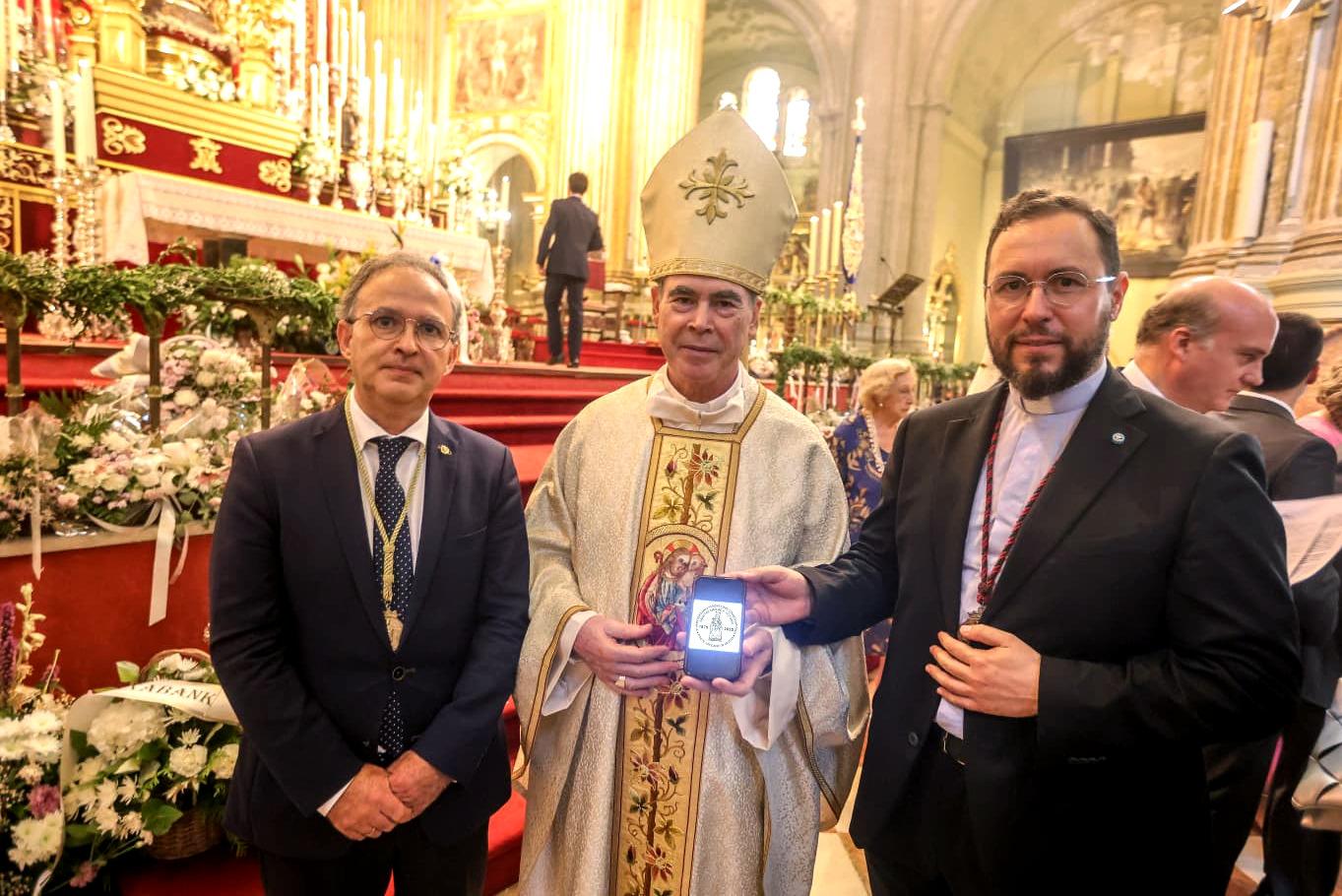 Mons. Jesús Catalá muestra el diseño del sello junto al hermano mayor de la Hermandad de la Victoria, Miguel Orellana, y el sacerdote Salvador Aguilera